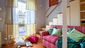 Ein gemütliches Zimmer mit einem roten Sofa, einer Treppe und Blick auf ein historisches Gebäude durch das Fenster.