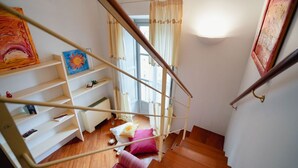 Eine Treppe mit Holzwandhandlauf, eine weiße Wand mit einem Gemälde und ein Fenster mit Vorhängen.
