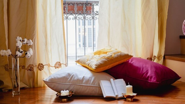 Ein Schlafzimmer mit Bett, einem Fenster mit Blick auf Gebäude, einer Vase mit Blumen und einer Kerze auf dem Nachttisch.