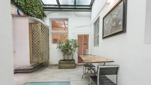 A narrow courtyard with a wooden table and chairs, a small pool, and a potted plant.