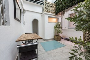 Un patio con una mesa y banca de madera, una planta en maceta y una ventana pequeña.