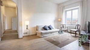 A modern living room with a sofa, coffee table, and chairs. There is a window with curtains, a lamp, and a plant.