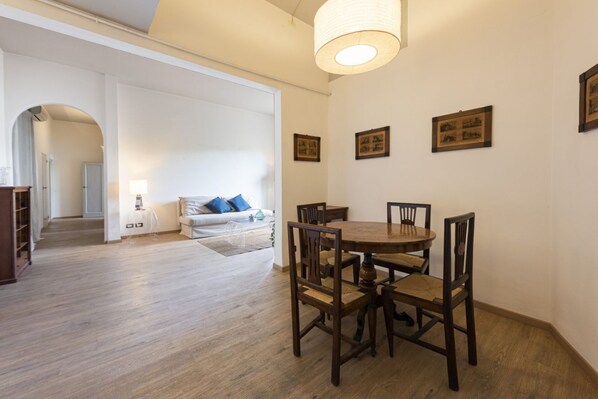 Un comedor con una mesa y sillas de madera, un sofá blanco con cojines azules, y un pasillo que conduce a otra habitación.