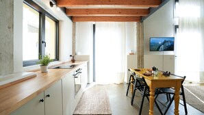 A modern kitchen with wooden beams, a dining area with a wooden table and chairs, and a TV mounted on the wall.