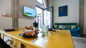 A dining area with a yellow table set for breakfast, a television mounted on the wall, and a blue sofa in the background.