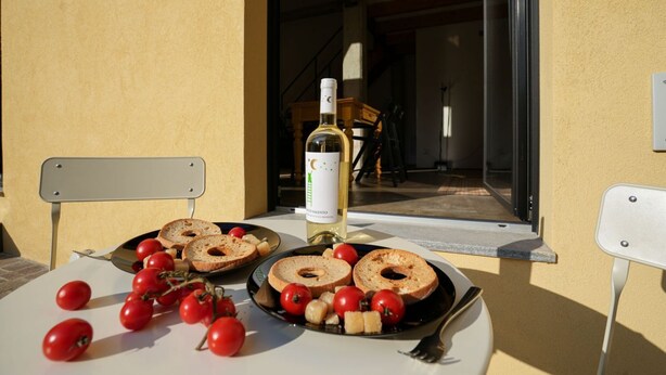 A table with bread, tomatoes, and a bottle of wine on a balcony.
