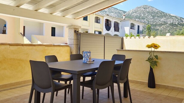 An outdoor patio with a table and chairs, a vase with flowers, and a mountain view. - [Casalinda] Apartment in Orosei with veranda (Orosei)