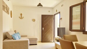 A living room with a sofa, a dining table with chairs, a television, and a door with a decorative pattern. - [Casalinda] Apartment in Orosei with veranda (Orosei)