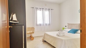 A bedroom with a bed, a window with curtains, a small wooden cart, and a sailboat decoration on the door. - [Casalinda] Apartment in Orosei with veranda (Orosei)