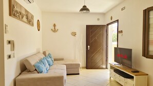 A living room with a beige sofa, a TV on a wooden stand, and a door leading to another room. - [Casalinda] Apartment in Orosei with veranda (Orosei)