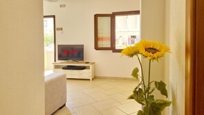 A living room with a TV displaying 'NETFLIX', a white sofa, and a sunflower in a vase. - [Casalinda] Apartment in Orosei with veranda (Orosei)