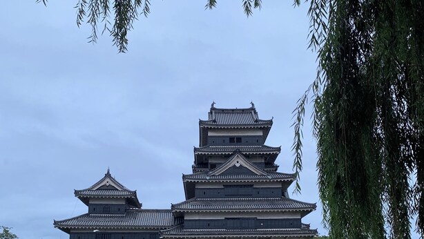 Eine traditionelle japanische Burg mit mehreren Geschossen, umgeben von einem Burggraben, der sich im Wasser spiegelt.