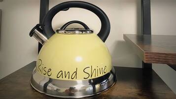 A yellow kettle with the inscription "Rise and Shine" on its base, placed on a wooden table against a wall.