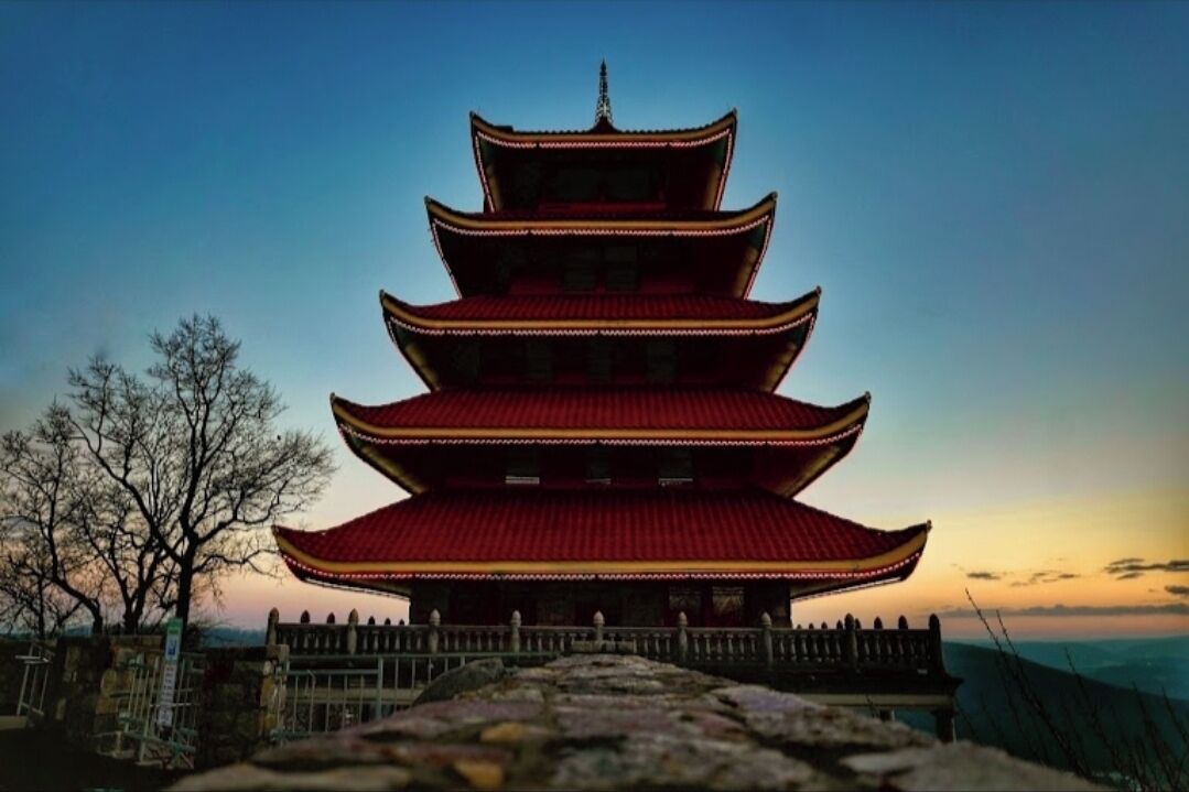 Une pagode traditionnelle à plusieurs niveaux, surmontée d’un toit rouge, se dressant sur fond de ciel crépusculaire.