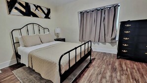 Un dormitorio con cama, mesita de noche, cómoda, ventana con cortinas y un cuadro en la pared.