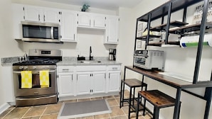 Una cocina con gabinetes blancos, electrodomésticos de acero inoxidable, una cafetera y una pequeña mesa de madera.