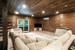 A wooden-paneled room with a large sofa, a flat-screen TV, and a sliding glass door leading outside.