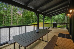 A covered outdoor deck with wooden benches and a barbecue grill. - Game Haven | Hocking Hills, Game Room, Hot Tub (McArthur)