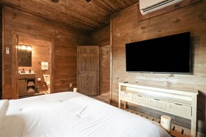 Une pièce en bois avec un lit, un téléviseur fixé au mur, une armoire en bois et un miroir.