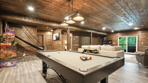 Una mesa de billar con bolas, un sofá y una lámpara colgante en una habitación con paredes y techo de madera.