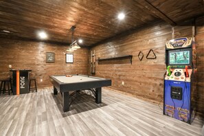 A pool table, a ping pong table, and a claw machine in a room with wooden walls and a wooden floor.