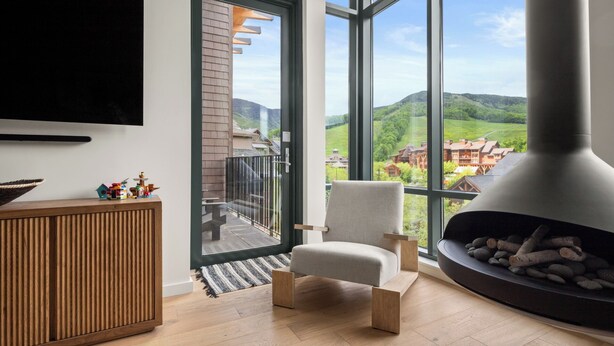 A modern living room with a large window, a fireplace, and a wooden cabinet. - Stowe Mt Resort | Spruce Peak | 4 Bed | Treehouse Condo | Sleeps 16 (Stowe)