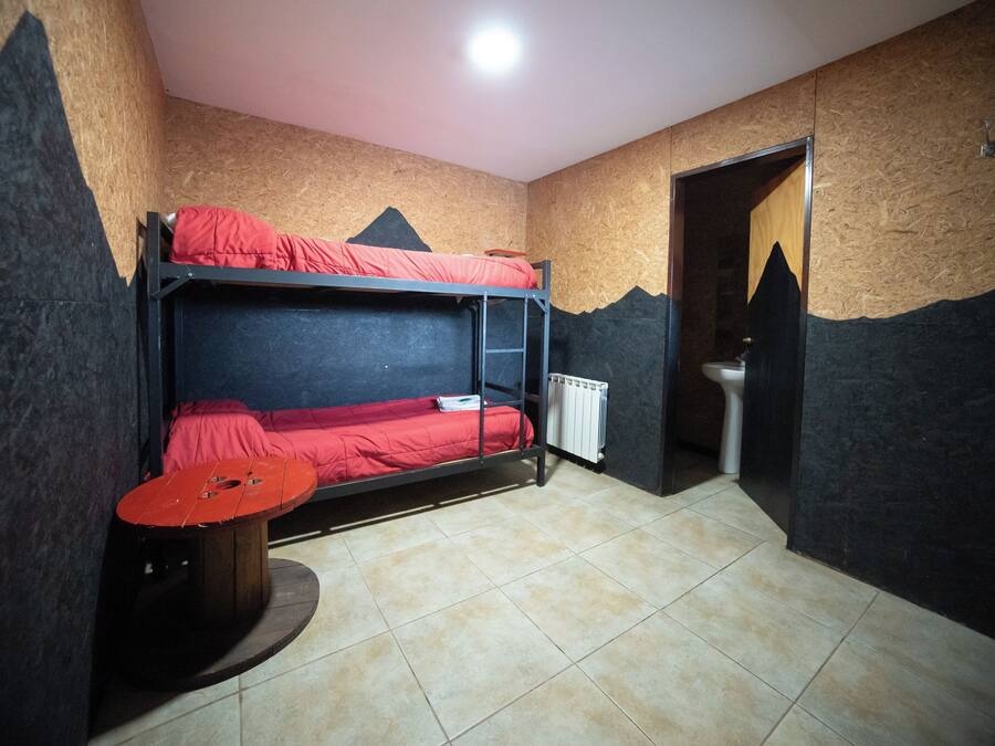 Una habitación con literas, un radiador, una mesita y una puerta que da a un baño.