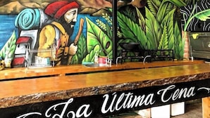 Interior de restaurant amb un mural que representa un xef i muntanyes, un taulell de fusta i llums penjants.