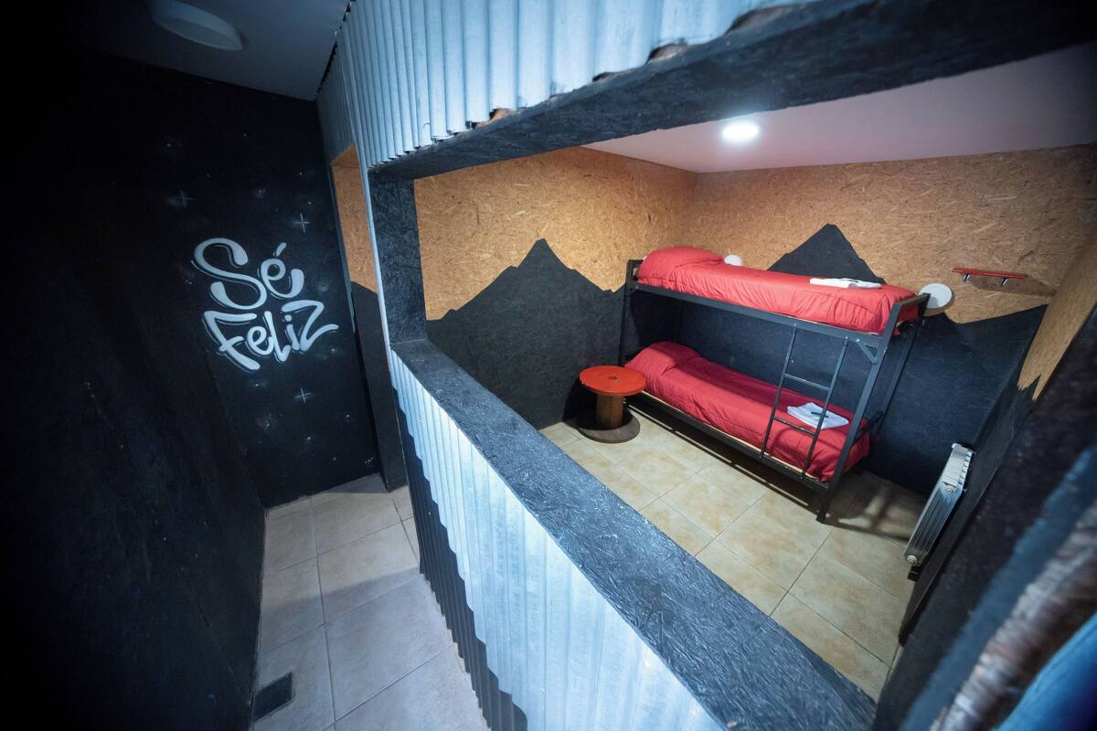 Habitación con literas, un mural de montaña en la pared y un grafiti que dice 'Sé Feliz'.