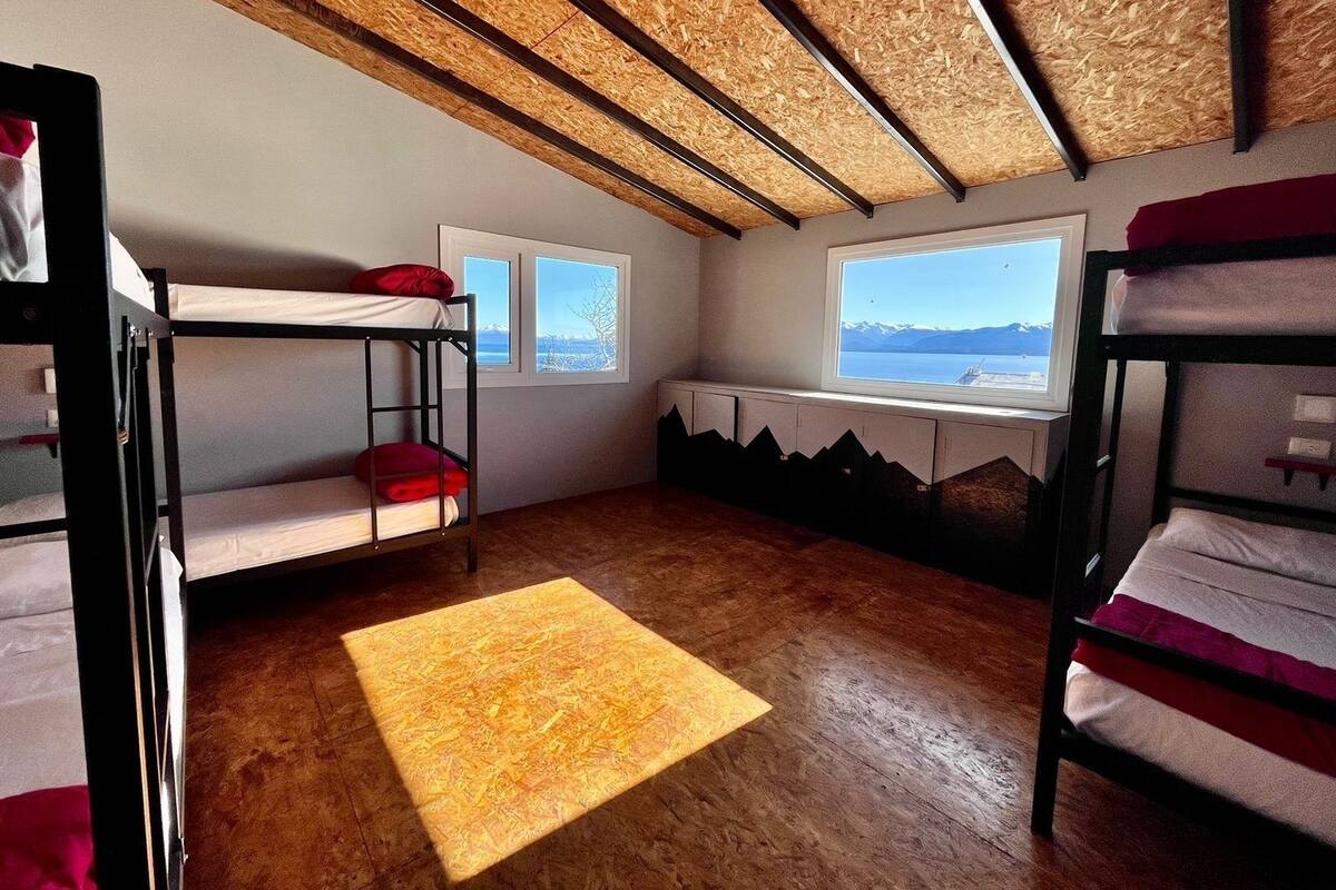 Un dormitorio con literas, pisos de madera, dos ventanas y vistas a la montaña.