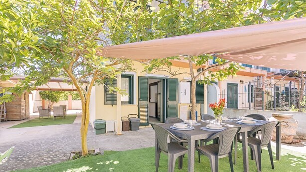 An outdoor dining area with a table set for four, surrounded by chairs, under a canopy. - Casa Catalpa near the beach (TORTOLI)