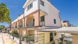 A two-story residential building with a balcony, a covered patio, and a small garden area. - Casa Catalpa near the beach (TORTOLI)
