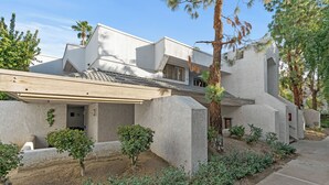 Une maison moderne avec un toit plat, de grandes colonnes en pierre et un petit jardin agrémenté d’arbustes et d’un arbre.