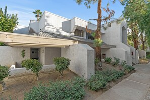 Una casa moderna con techo plano, amplias columnas de piedra y un pequeño jardín con arbustos y un árbol.