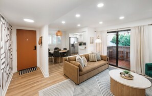 A modern living room with a sofa, a dining area, and a kitchen in the background.