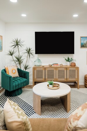 Een moderne woonkamer met een groene bank, een ronde salontafel en een grote flatscreen televisie aan de muur.