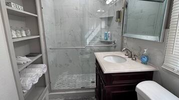 Une salle de bain avec une douche à parois de verre, un meuble-lavabo avec un miroir et des toilettes.