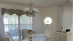 Un comedor con una mesa de vidrio, sillas a rayas, una araña y vistas al exterior a través de ventanas amplias.