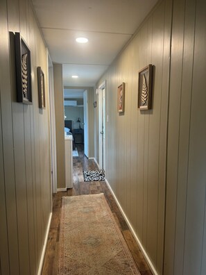 Stylish hallway leads to a room with a kitchen area, featuring a patterned rug and framed artwork.