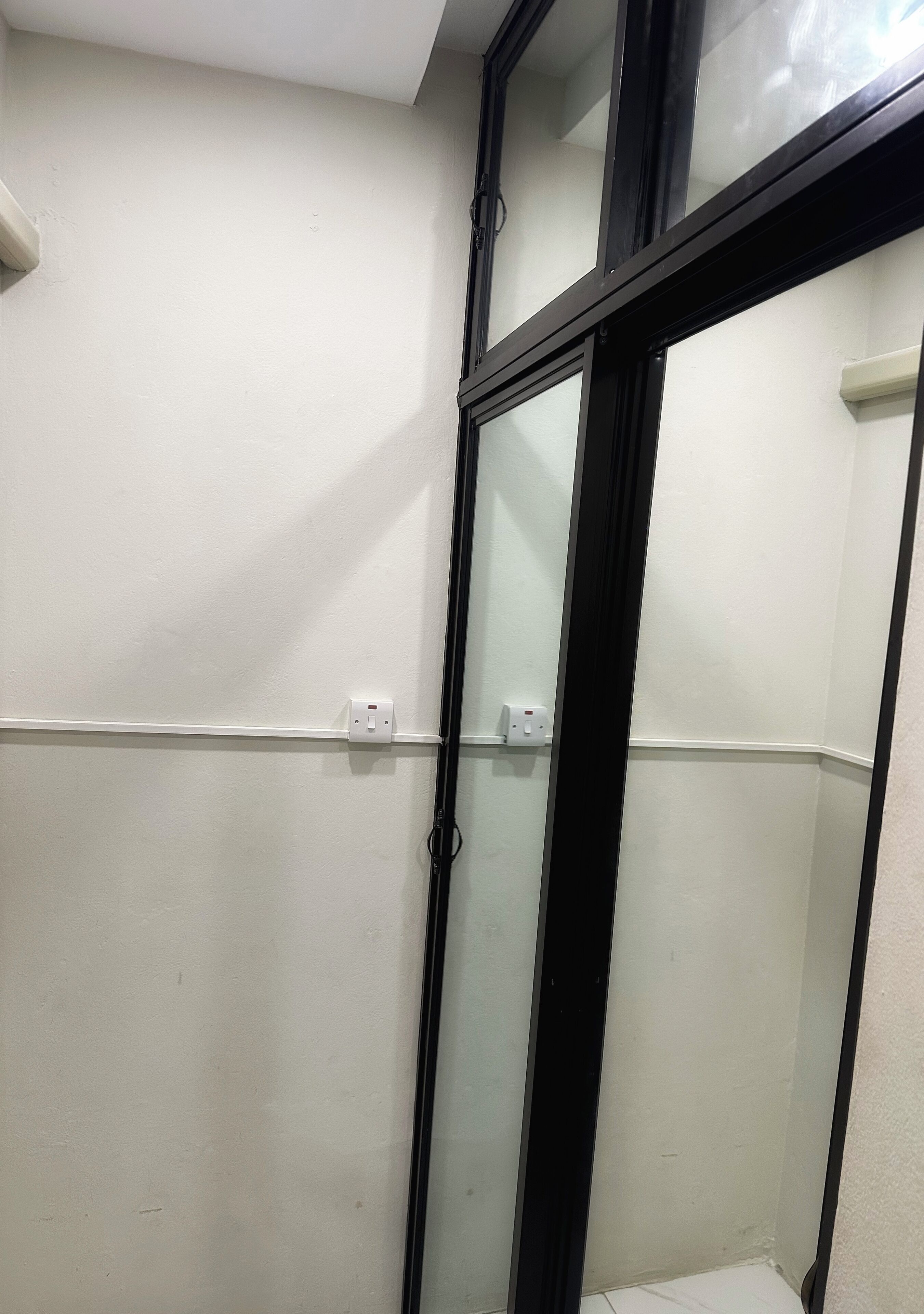 A corner of a room with a white wall, a black-framed window, and a white electrical outlet.