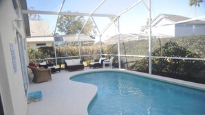 A swimming pool with a curved edge, surrounded by a covered patio with lounge chairs and a small table. - "NEW to MARKET" <br>Charming 3-Bedroom, 2-Bath Vacation Home in Quiet Gated Community (Davenport)