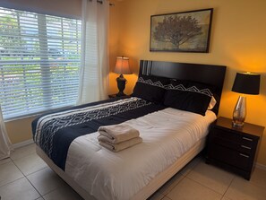 A neatly made bed with a patterned bedspread, a headboard, and a nightstand with a lamp.