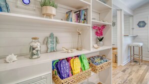Una habitación bien organizada con estantes blancos que contienen libros, objetos decorativos y chanclas.