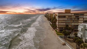 Um hotel à beira-mar com vários andares, uma praia de areia e ondas do oceano.