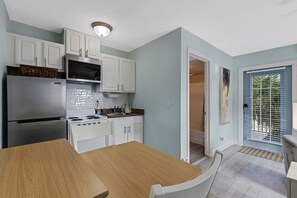 A modern kitchen with white cabinets, a stainless steel refrigerator, and a wooden dining table. - ☀️Sunset Corner - Beach View Suite | Heated Pool • Across from Beach ➠ 16333 Gulf Blvd 215 (Redington Beach)
