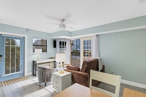A room with a dining table, chairs, a sofa, a lamp, and a ceiling fan. - ☀️Sunset Corner - Beach View Suite | Heated Pool • Across from Beach ➠ 16333 Gulf Blvd 215 (Redington Beach)