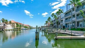 A waterfront hotel with multiple balconies, a dock, and palm trees. - 108 1st Floor ! Waterfront !  Pool ! Hot ! Tub   (Corpus Christi)