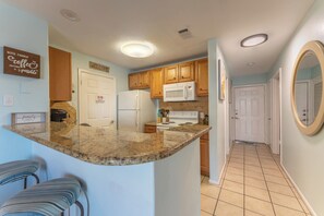 A kitchen with granite countertops, wooden cabinets, a white refrigerator, and a microwave. There are two bar stools and a sign on the wall. - 108 1st Floor ! Waterfront !  Pool ! Hot ! Tub   (Corpus Christi)