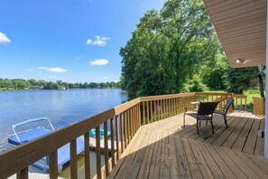 Une terrasse en bois offrant une vue sur un lac, un bateau amarré sur l’eau et une chaise.