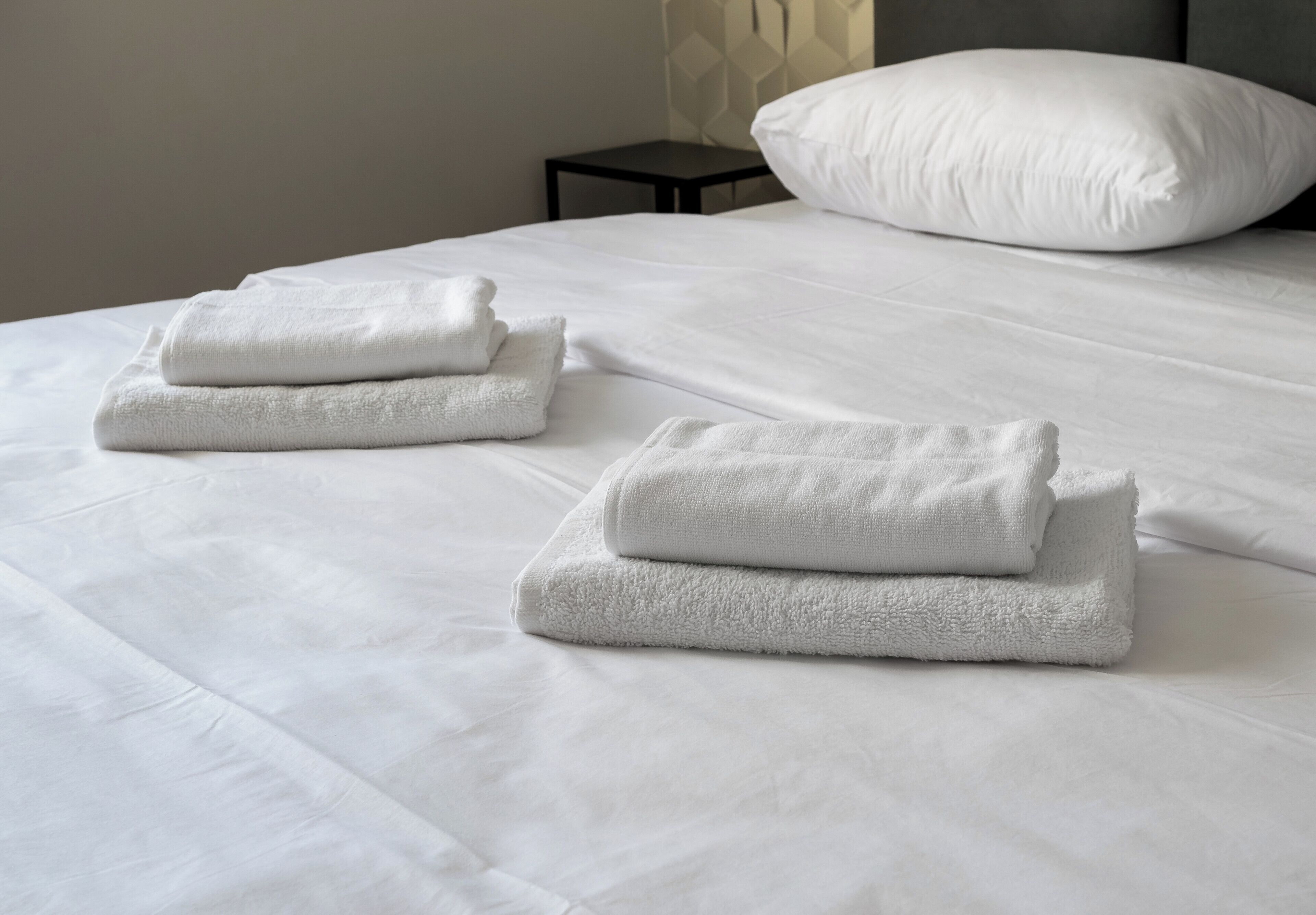 Una cama bien hecha con sábanas blancas y dos toallas dobladas sobre ella.